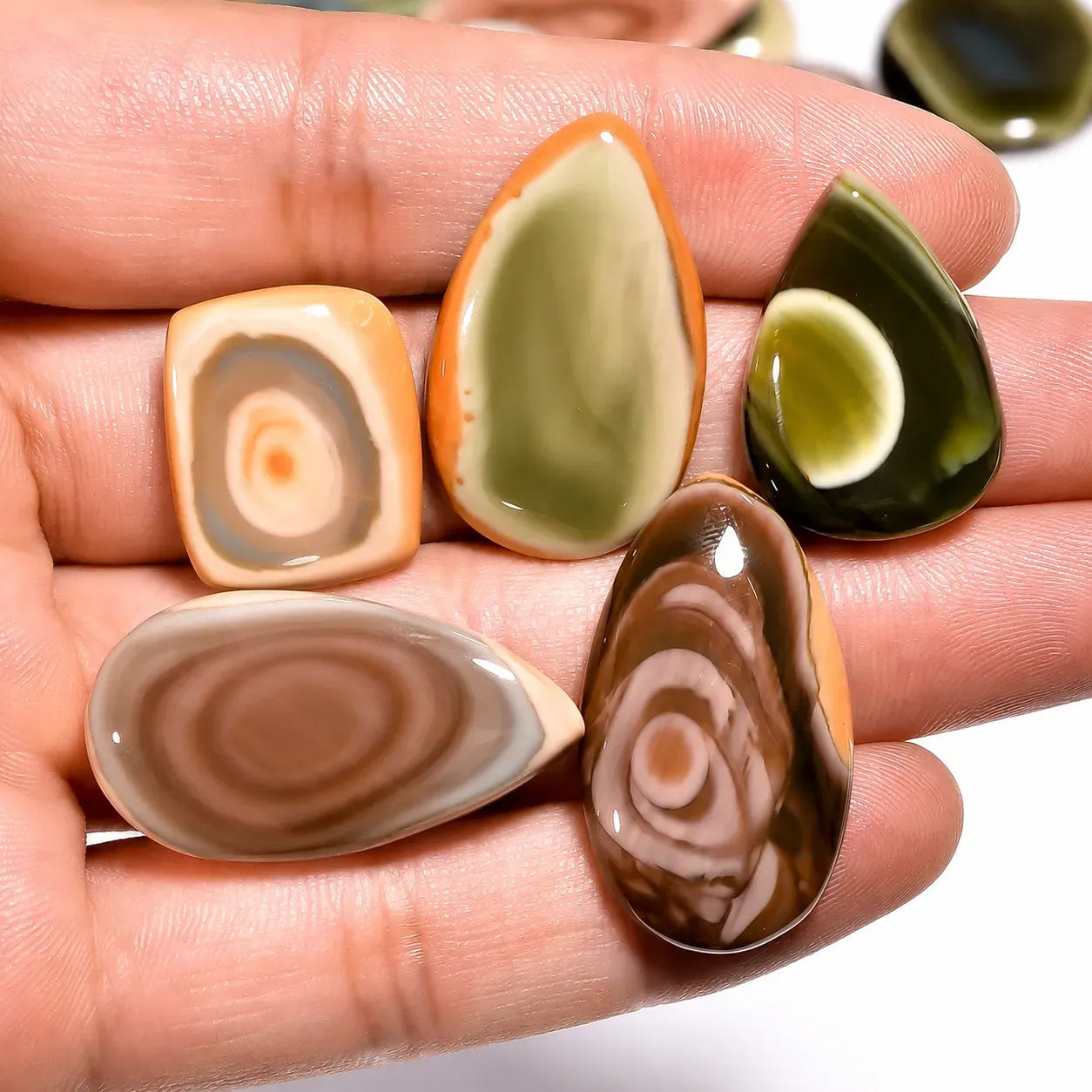 Five polished stones with swirl patterns held in a hand against a white background