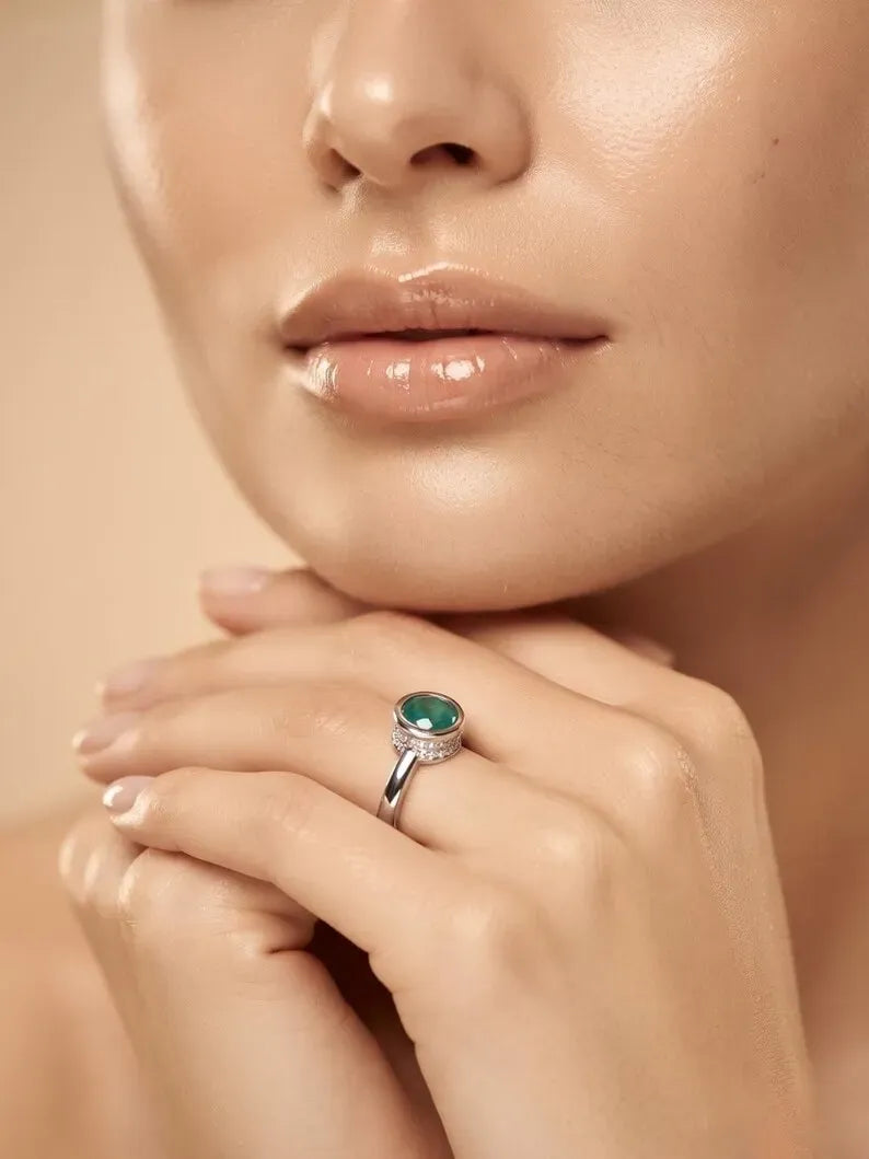 Woman wearing a 925 sterling silver ring with a round green stone and CZ accents, hands resting under her chin