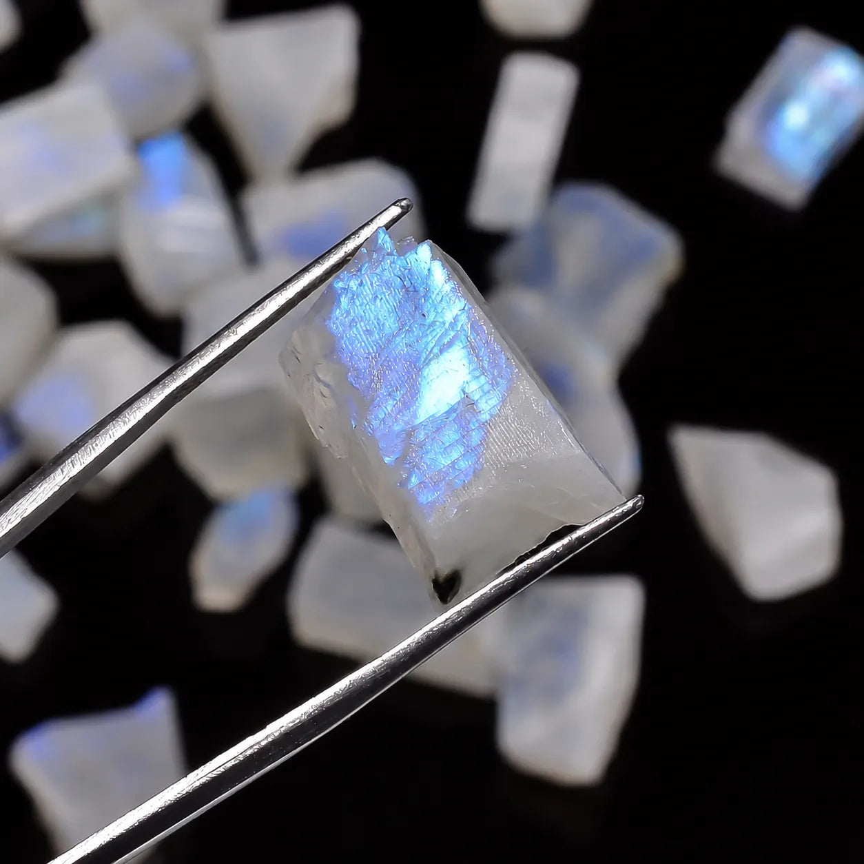 Opal stone with a blue glow held by tweezers against a dark background