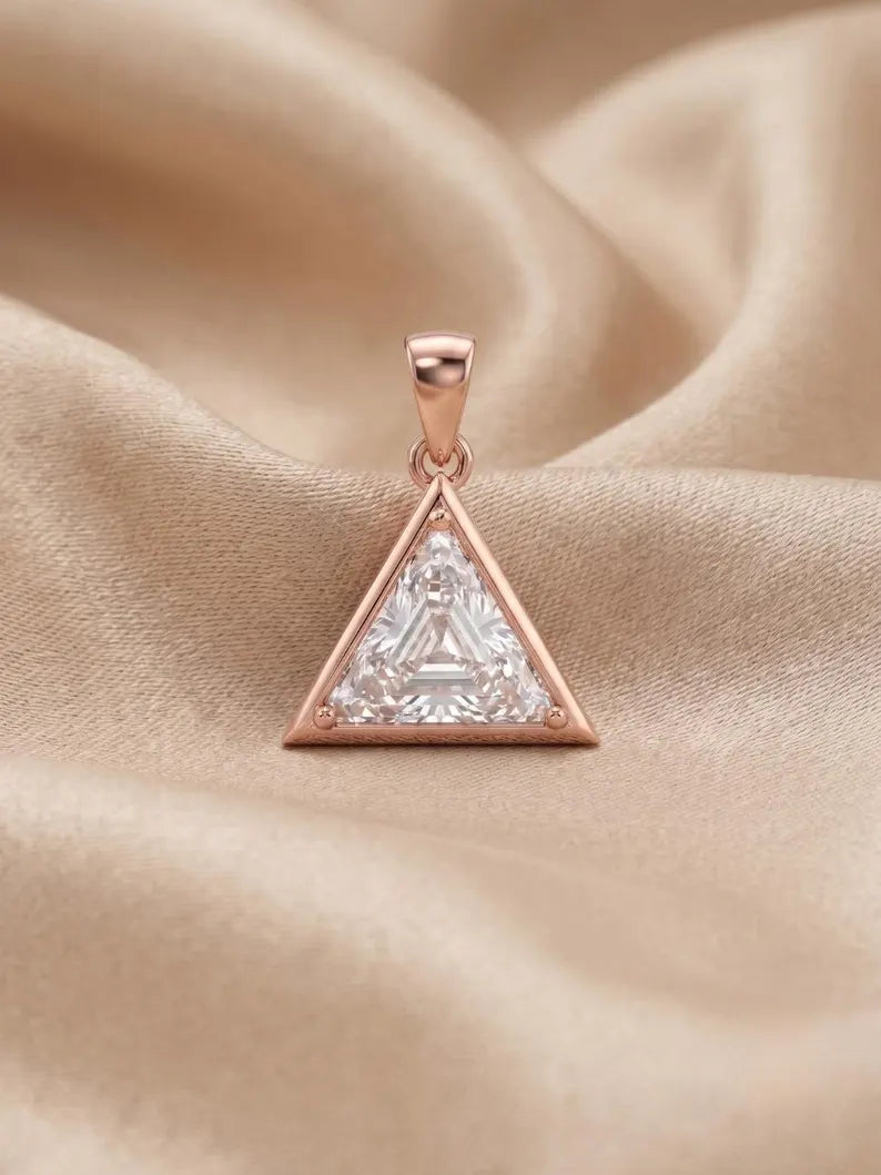 A rose gold triangle pendant featuring a clear triangular gemstone, resting on a draped beige satin fabric background.