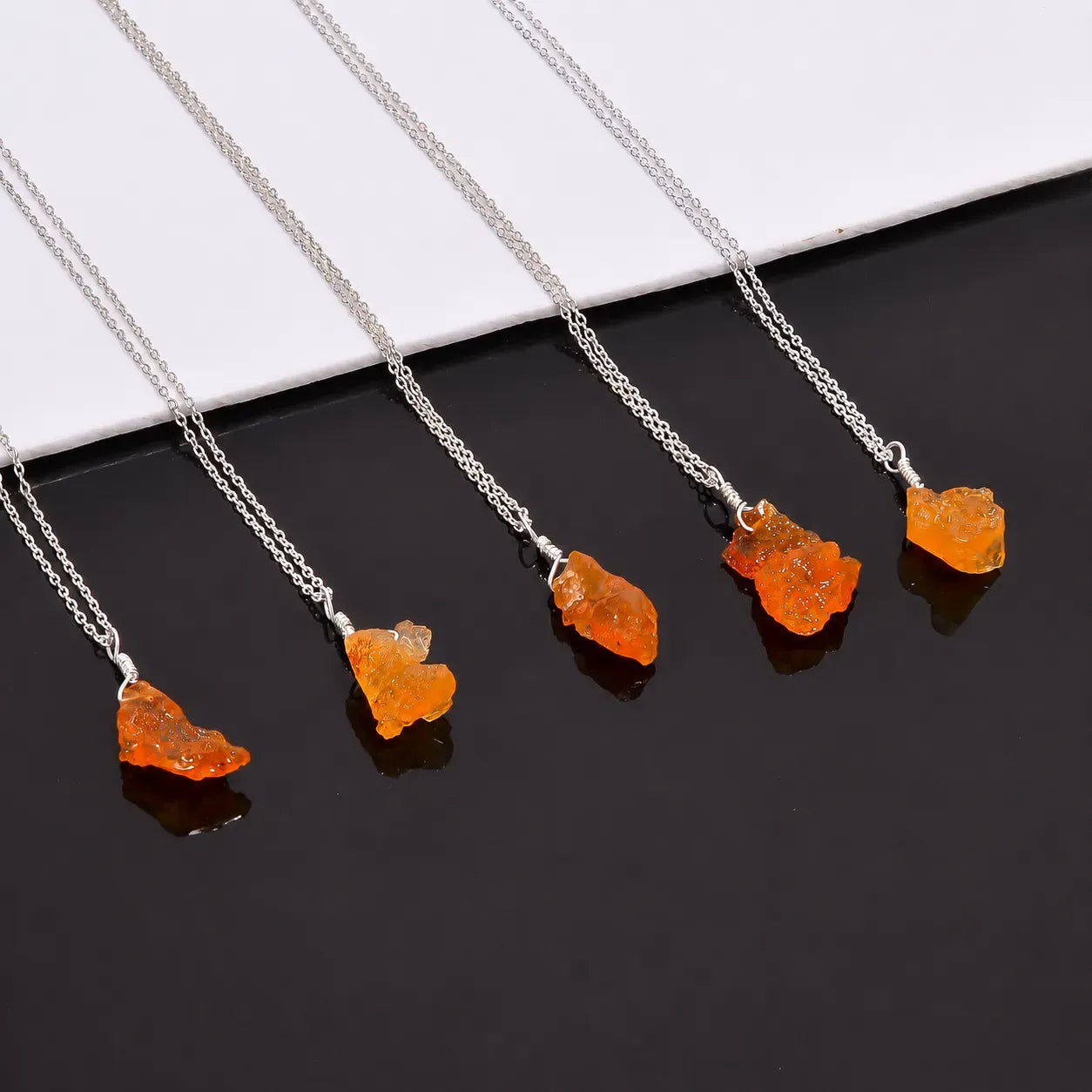Silver necklaces with orange pendant stones on a black and white background