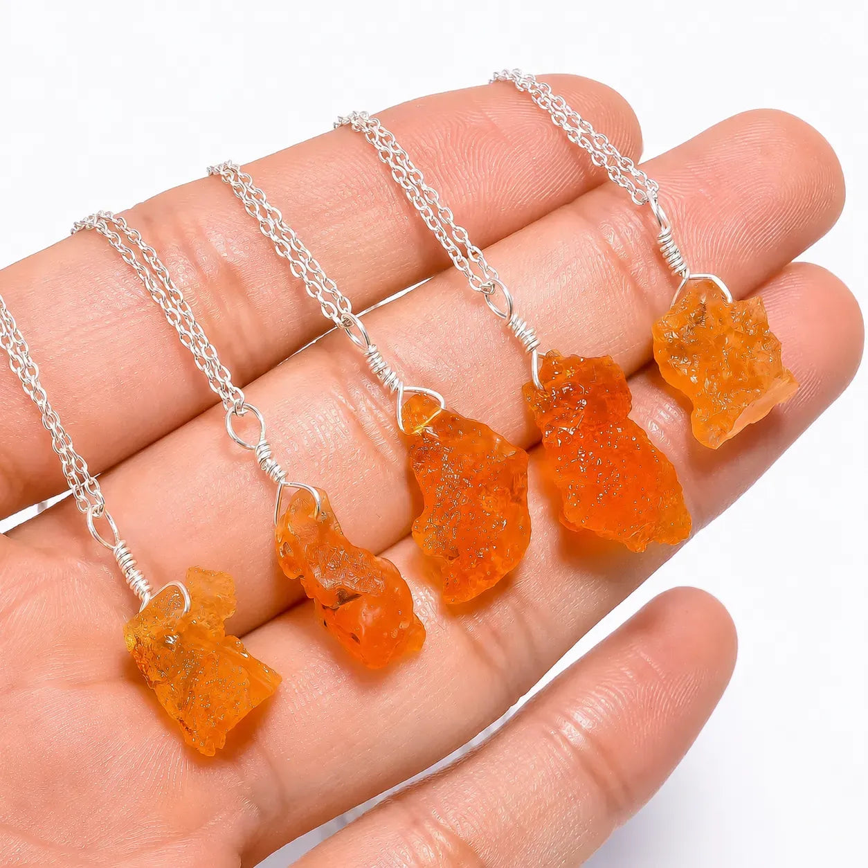 Orange butterfly-shaped pendants on silver chains held in a hand against a white background