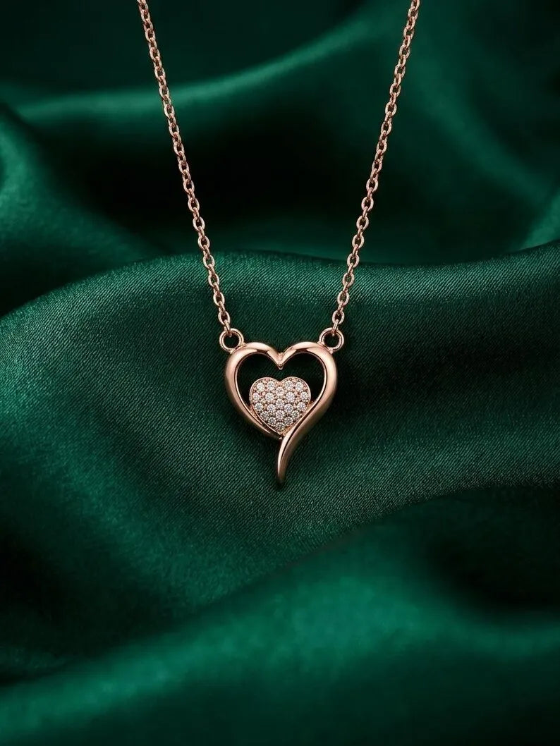 A rose gold heart pendant necklace with a pavé-set heart in the center, displayed on a draped dark green satin fabric background.
