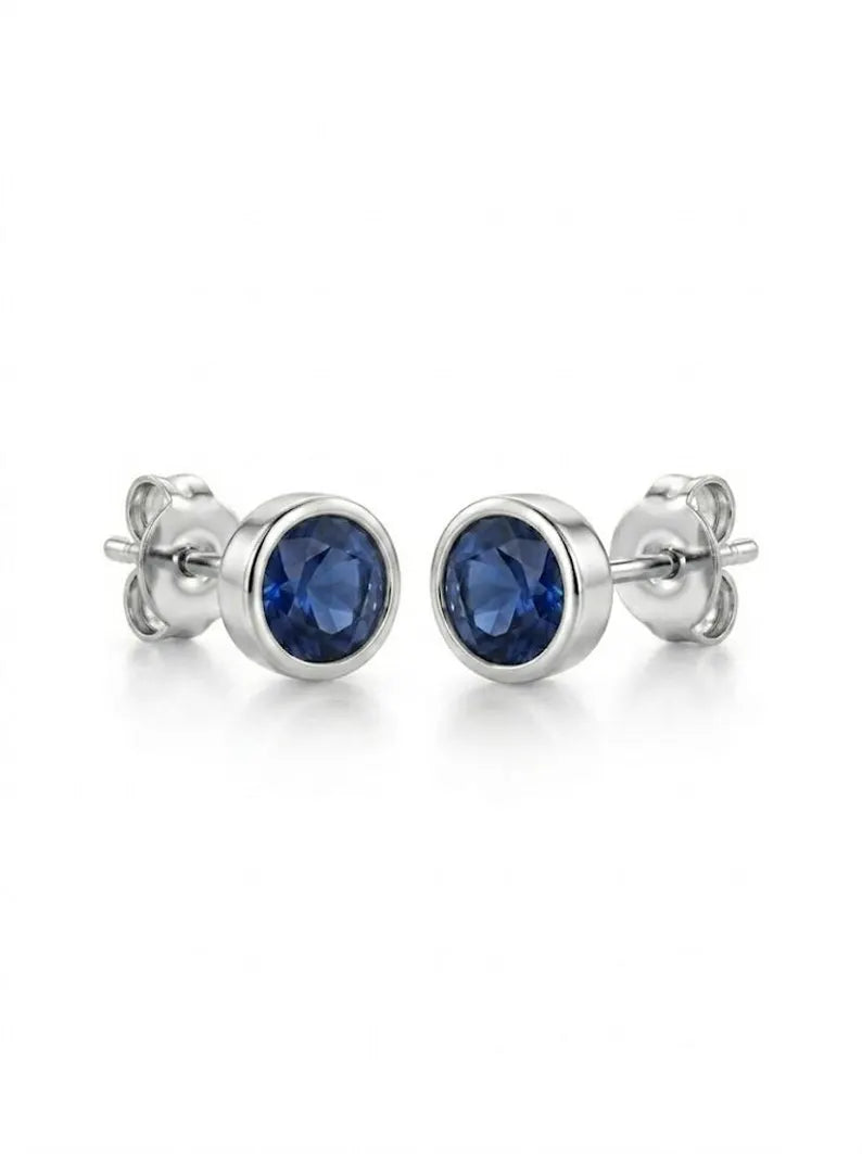 A pair of silver stud earrings with round-cut deep blue gemstones, displayed on a clean white background.