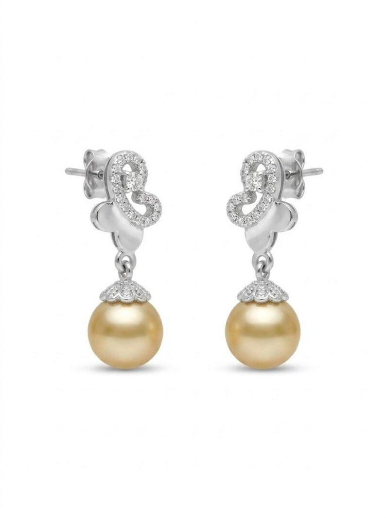 A pair of silver drop earrings featuring a pavé-set crystal scrollwork top and a dangling round gold pearl at the bottom, shown on a plain white background.