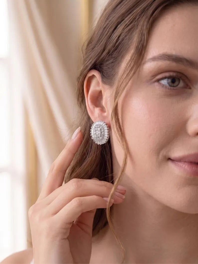 A close-up lifestyle shot of a woman wearing a round silver-toned stud earring adorned with clear crystals, with her hand gently touching her hair.
