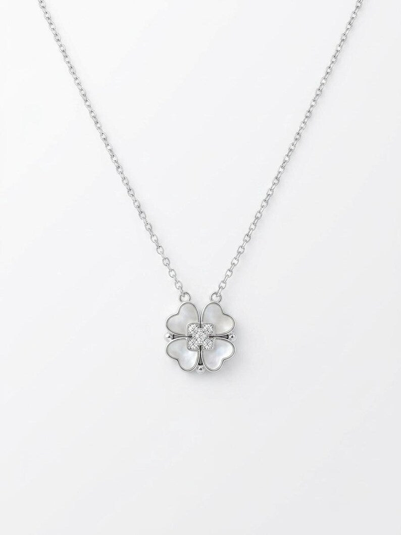A silver necklace featuring a small flower pendant with four heart-shaped petals and a central clear crystal, displayed on a clean white background.