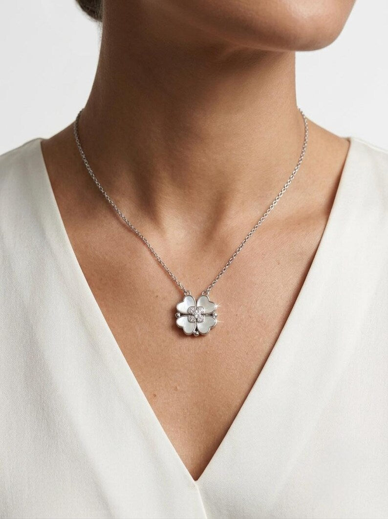 A close-up of a model wearing a delicate silver chain necklace with a small silver flower-shaped pendant, paired with a white V-neck top.