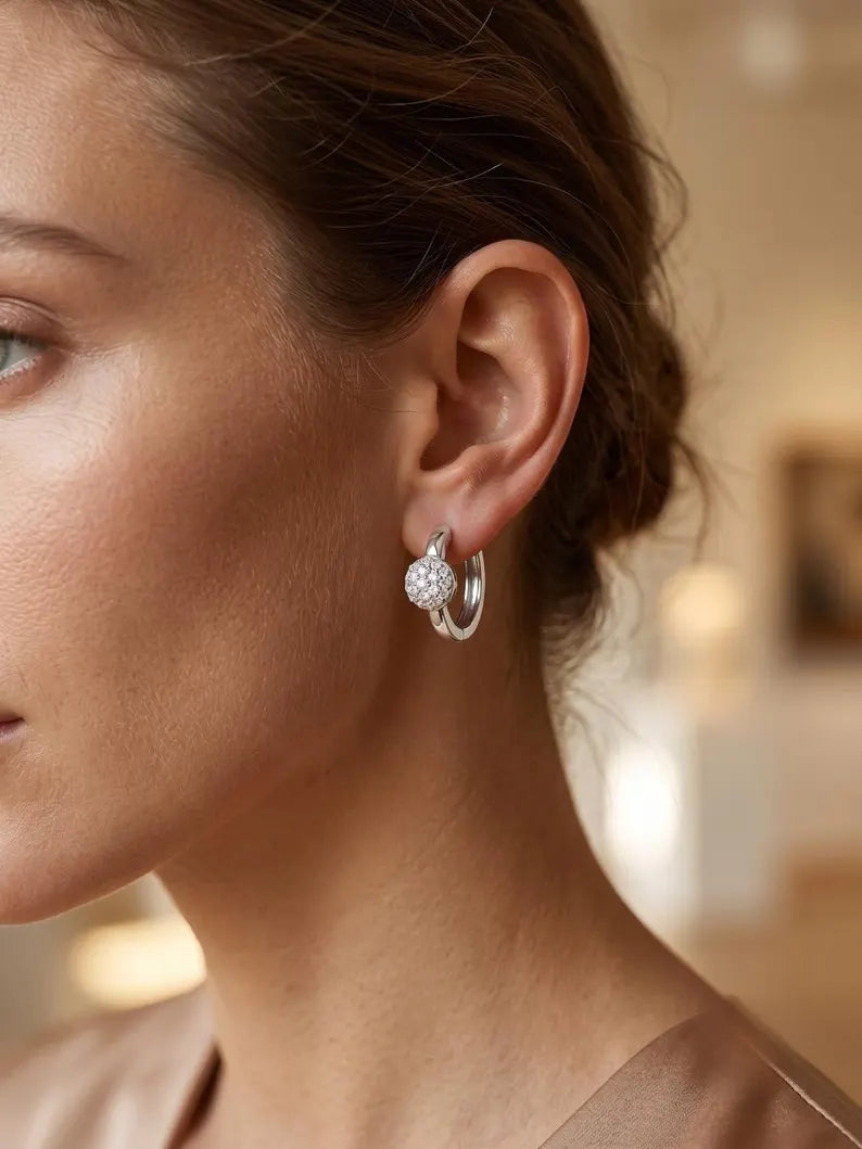 A close-up side profile of a woman wearing a silver hoop earring adorned with a small, round, diamond-like crystal cluster at the front.