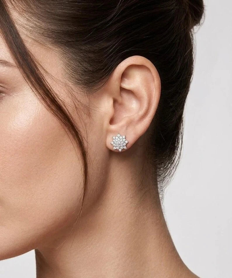 A close-up side profile of a woman wearing a small, round cluster stud earring in a silver-toned setting with clear stones.