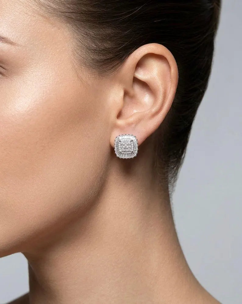 A close-up side profile of a woman wearing a small square stud earring with a silver-toned double-row setting of clear stones.