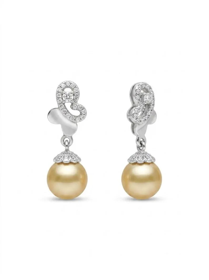 A pair of silver drop earrings featuring a small cluster of clear pavé stones in an abstract curved shape above a large round gold pearl, set against a plain white background.