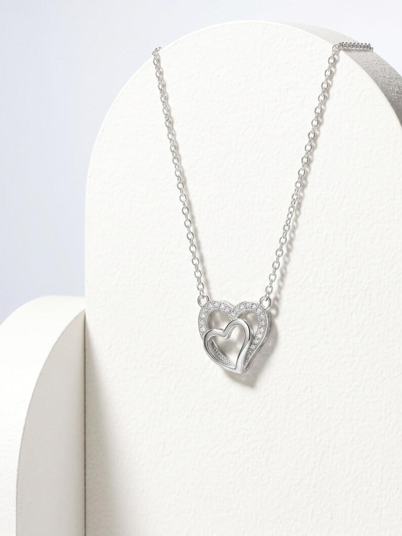 A silver double-heart pendant necklace displayed on a white jewelry bust against a light gray background.