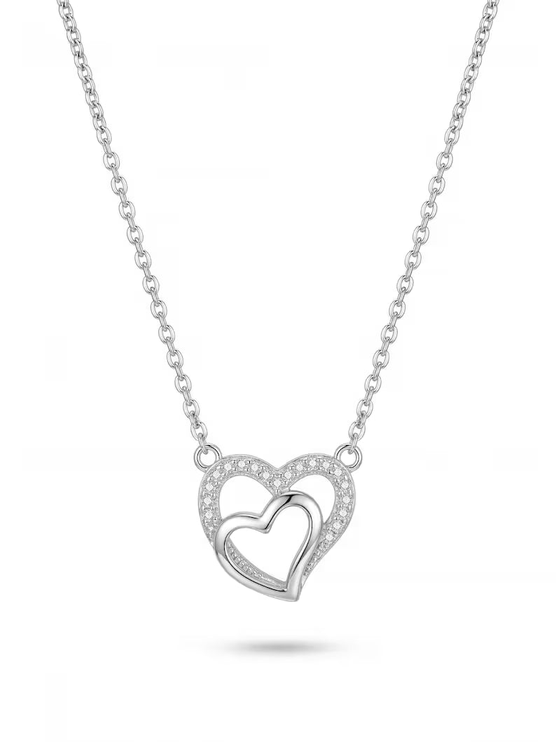 A silver-toned necklace featuring a double-heart pendant, with one heart fully open and the other partially enclosed by a halo of small clear stones, shown on a white background.