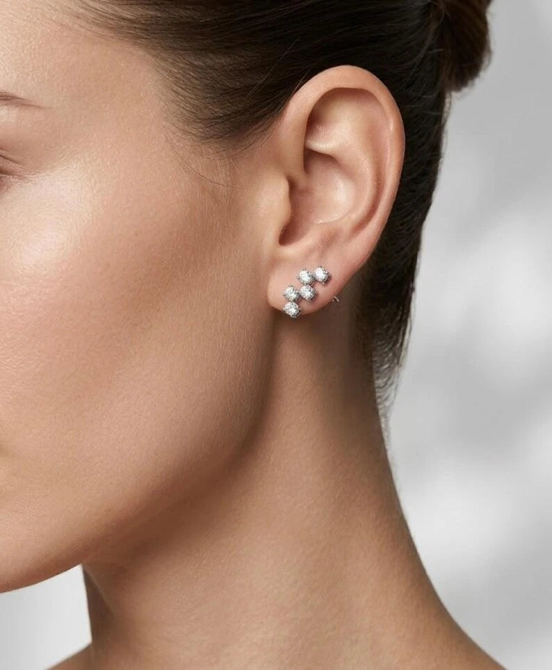 A close-up side profile of a woman's ear wearing a small cluster stud earring with sparkling clear stones in a silver-toned setting.