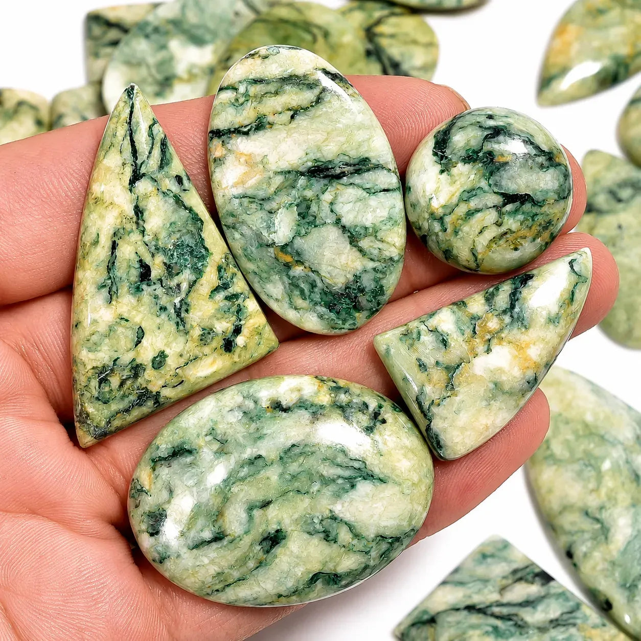 Hand holding green and white marbled stones with more stones in the background