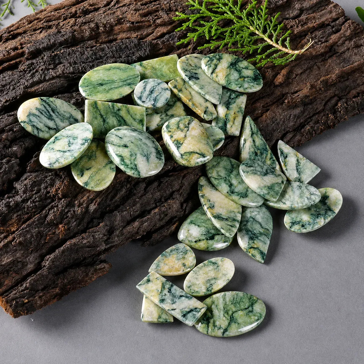 Green marbled stones on a gray surface with wooden logs and greenery.