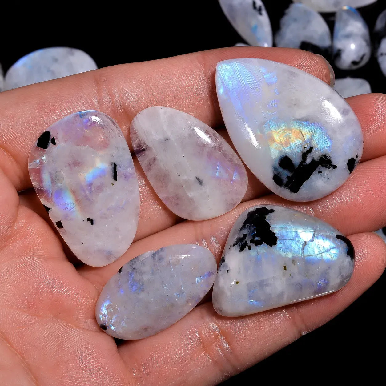 Opal stones with rainbow-like iridescence held in a hand against a dark background