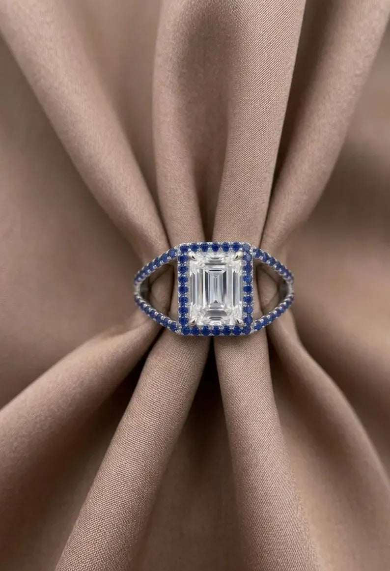 Front view of 925 sterling silver split shank ring with emerald cut center stone and blue CZ halo
