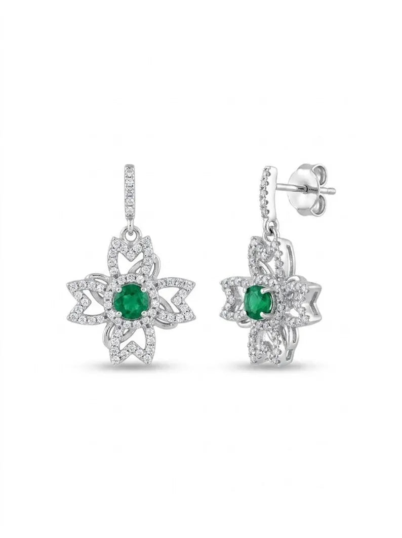 A pair of silver-toned dangle earrings featuring a central round green emerald stone surrounded by a halo of small clear pavé stones, with a matching green stone at the center of the starburst design. The earrings are shown against a plain white background, with one earring facing forward and the other angled to show the post and butterfly back.