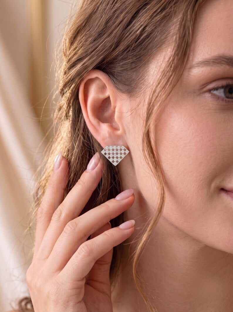 A close-up of a woman wearing a small geometric stud earring with a white and beige houndstooth pattern, touching her ear with her hand.