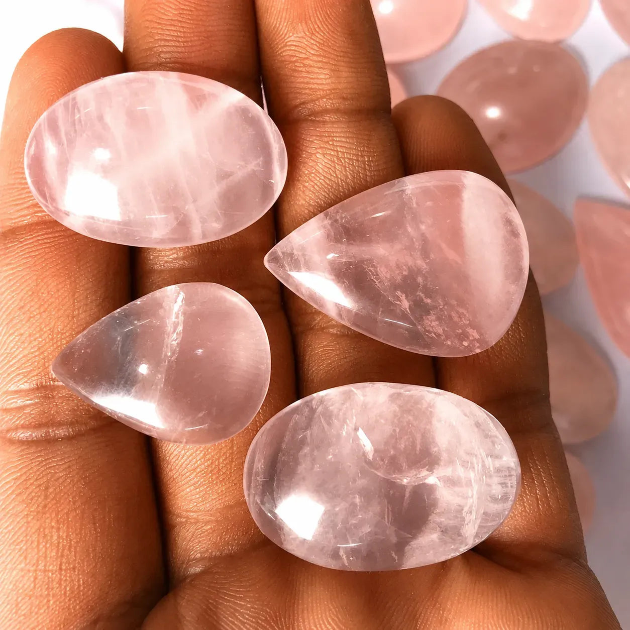 Four pink teardrop-shaped stones held between fingers with a blurred background of more stones.