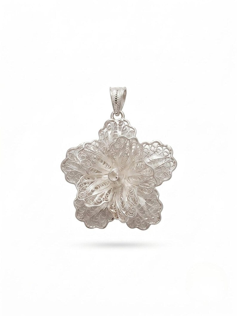 A silver-toned floral pendant with intricate filigree detailing and a small central pearl, shown against a plain white background.