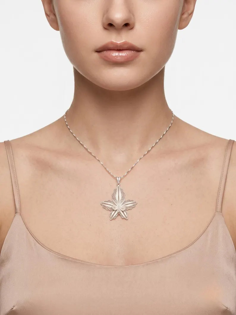 A close-up of a model wearing a delicate silver chain necklace with a textured, starburst-like silver pendant, styled with a beige camisole top against a clean white background.