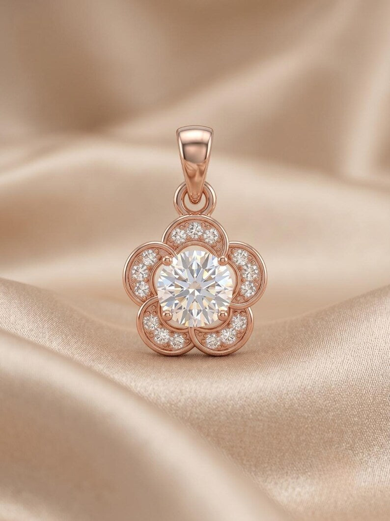A rose gold flower-shaped pendant with a central round clear gemstone and smaller accent stones, displayed on a draped beige satin fabric background.