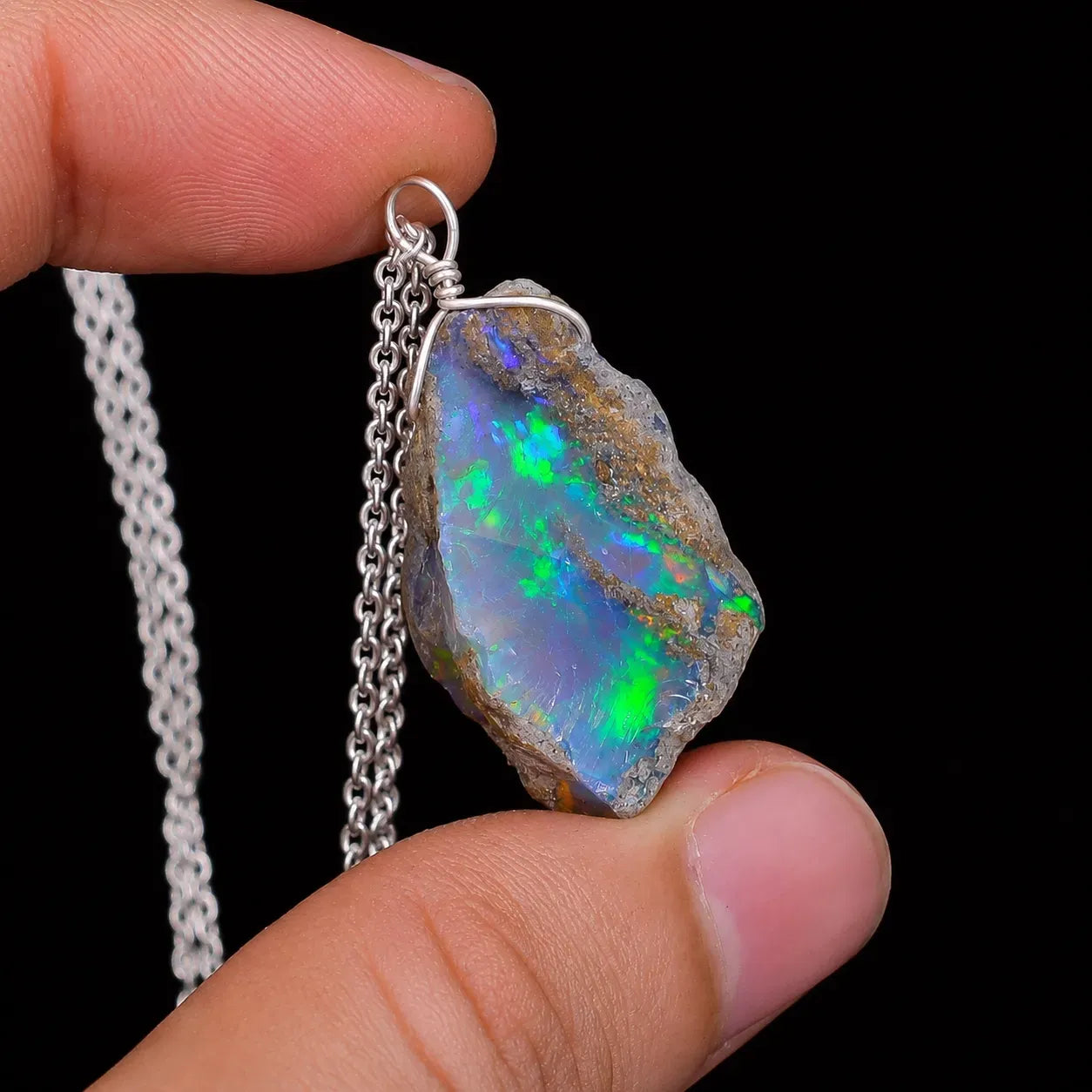 Opal pendant on a chain held between fingers against a black background