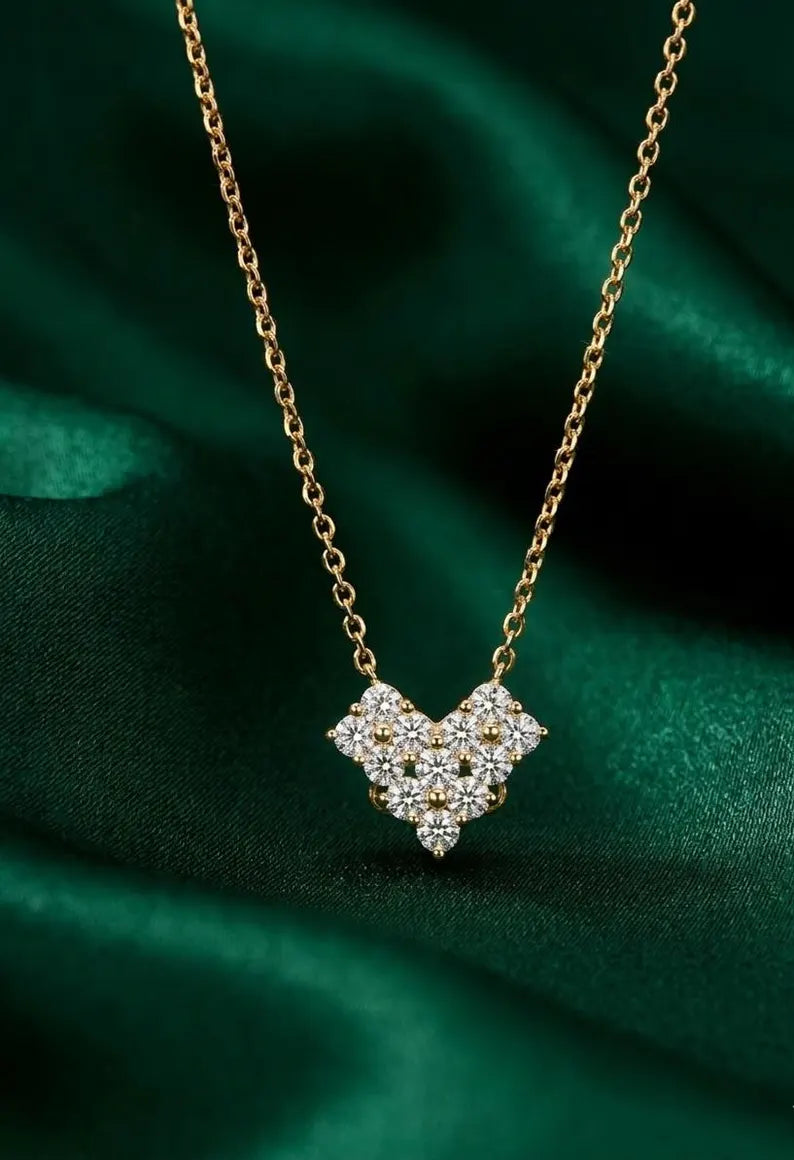 A gold chain necklace with a pavé diamond pendant in a heart shape, displayed on a draped dark green satin fabric.