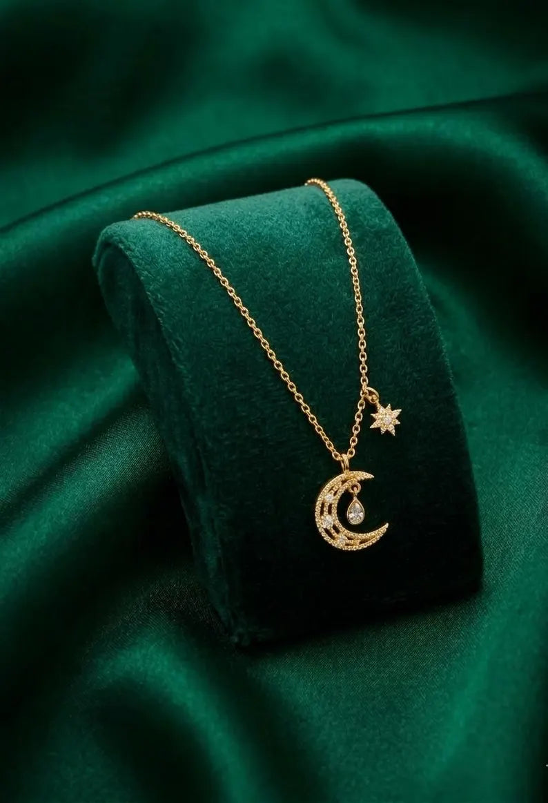 A gold crescent moon and star pendant necklace displayed on a dark green velvet jewelry stand against a matching green satin fabric background.