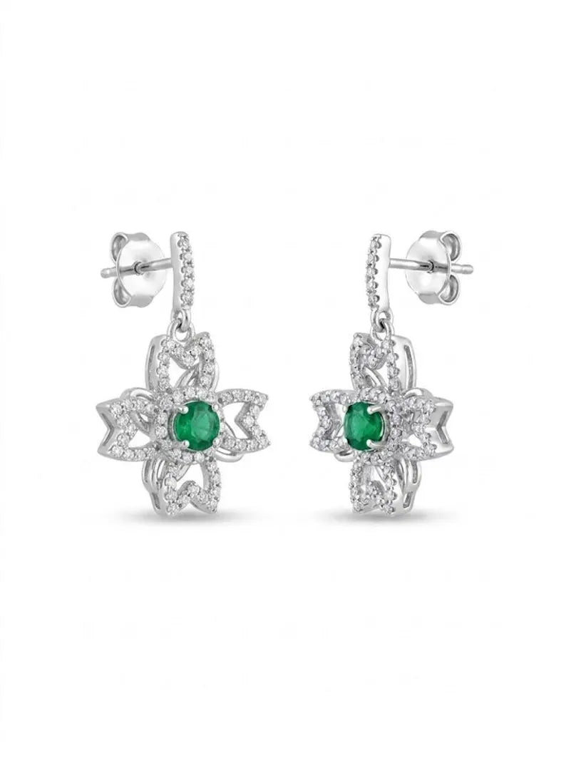 A pair of silver dangle earrings featuring a central round green emerald stone surrounded by a floral halo of small clear stones, shown against a plain white background.