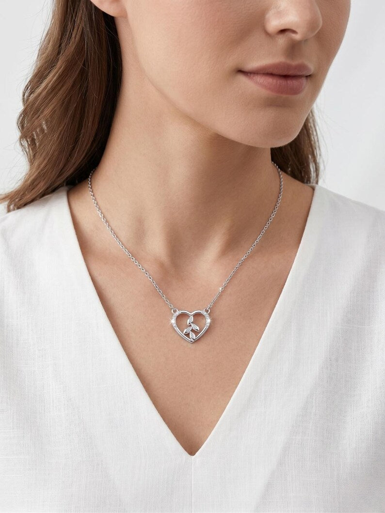 A close-up of a woman wearing a delicate silver necklace with a heart-shaped interlocking pendant, styled with a white V-neck top.