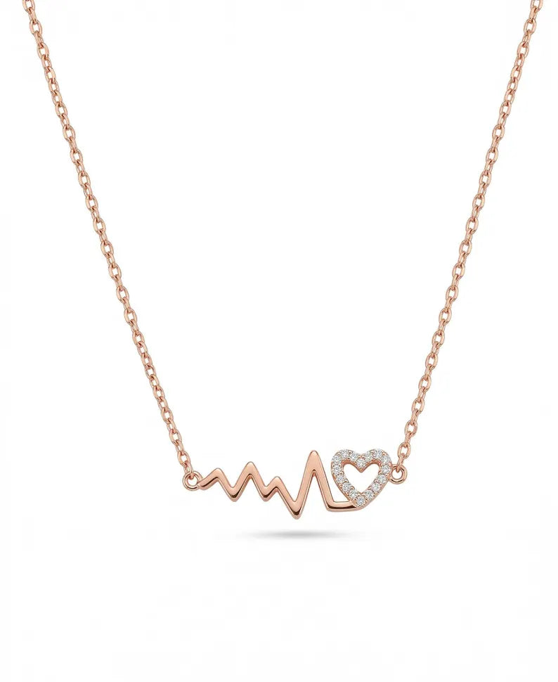 A delicate rose gold necklace featuring an EKG-style heartbeat pendant with a small heart-shaped cluster of clear stones, shown against a plain white background.