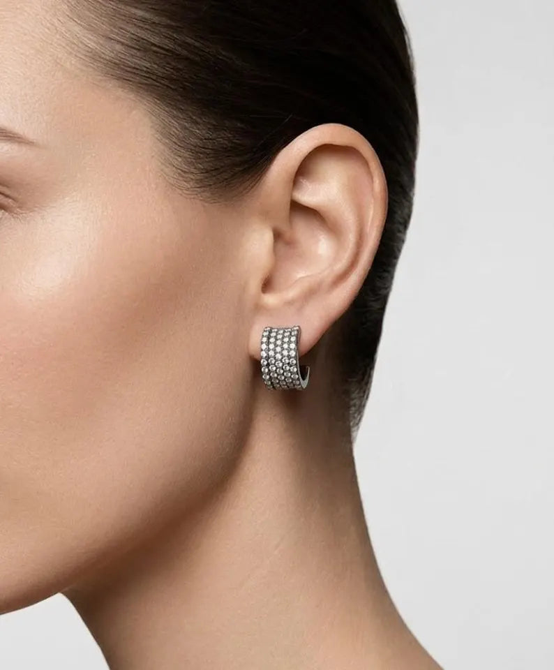 A close-up of a model's ear wearing a silver hoop earring adorned with multiple rows of small clear stones.