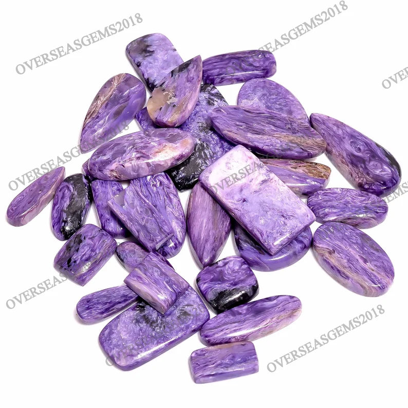 A pile of polished purple chrysocolla gemstone chips with natural marbled patterns in shades of purple, pink, and black, arranged on a white background with diagonal watermarks.