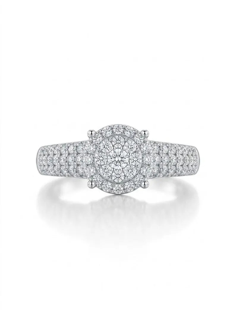 A silver-toned diamond halo ring with a round center stone and pavé-set band, shown on a clean white background with a soft reflection below.