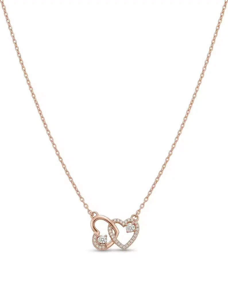 A delicate rose gold chain necklace featuring two interlocking open heart pendants, one adorned with a small clear gemstone, set against a plain white background.
