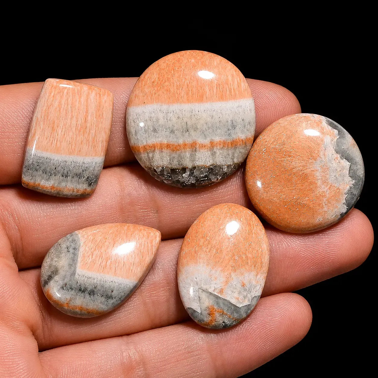 Five polished stones with a striped pattern held in a hand against a black background
