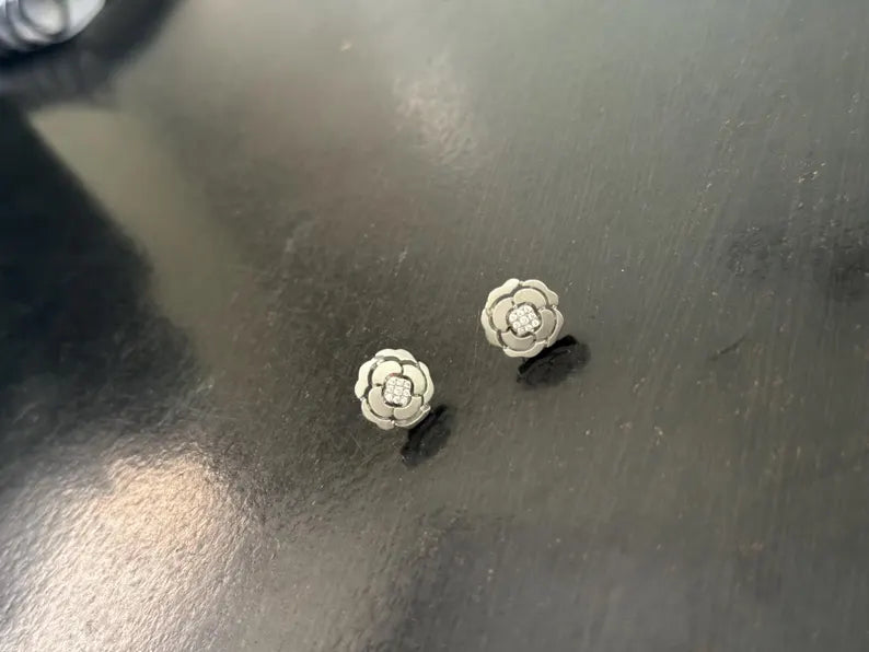 A pair of small silver flower-shaped stud earrings resting on a dark, reflective surface.