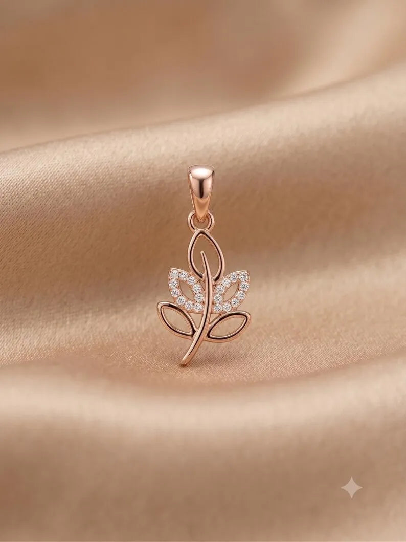 A rose gold leaf-shaped pendant with a small cluster of clear stones on one leaf, displayed on a draped beige satin fabric background.