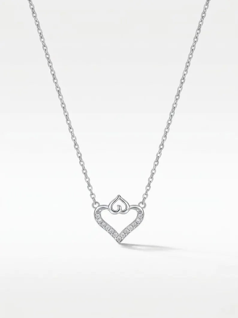 A silver heart-shaped pendant necklace with a pavé diamond outline and a small crown motif at the top, suspended from a delicate link chain against a clean white background.