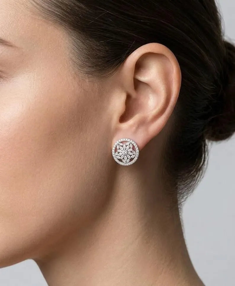 A close-up side profile of a woman's ear wearing a round Marquise floral halo stud earring with an intricate floral filigree pattern and a halo of small clear stones.