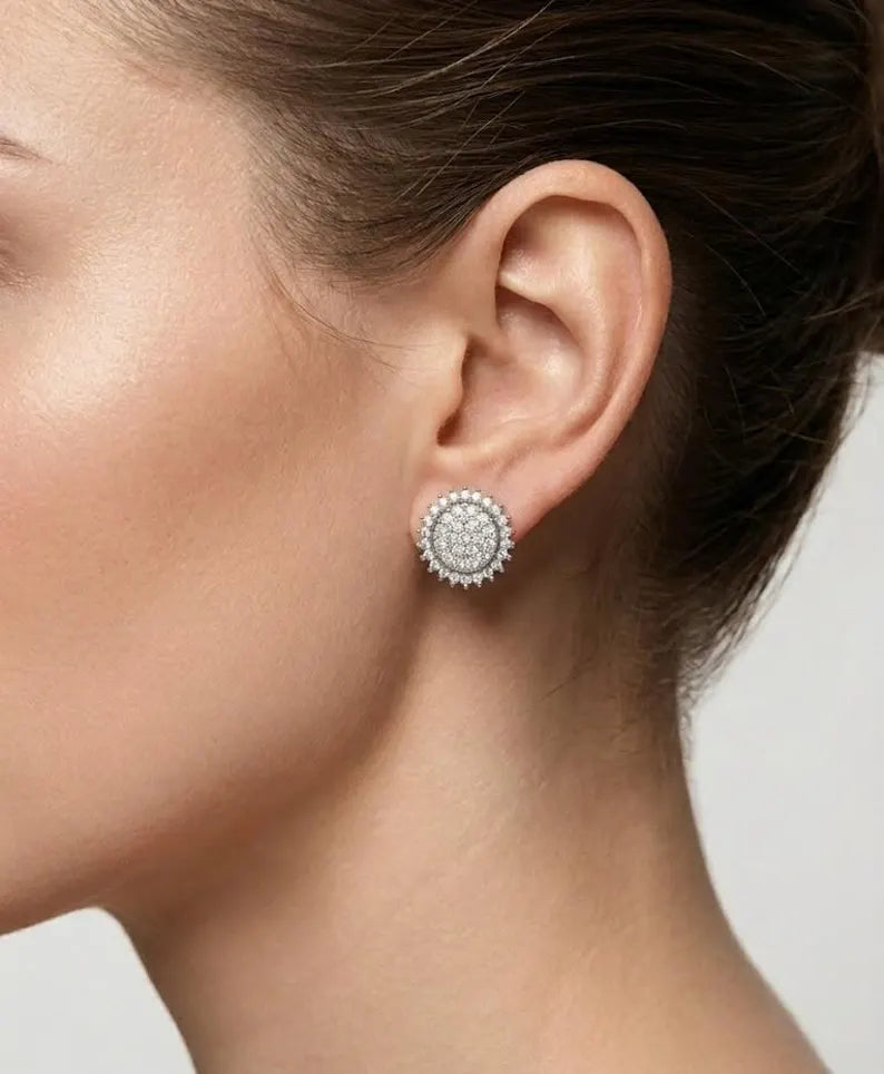 A close-up side profile of a woman's ear wearing a round silver stud earring with a halo of small clear stones.
