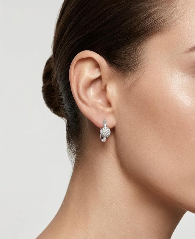 A close-up side profile of a woman's ear and neck wearing a small silver hoop earring with a textured, diamond-like surface.