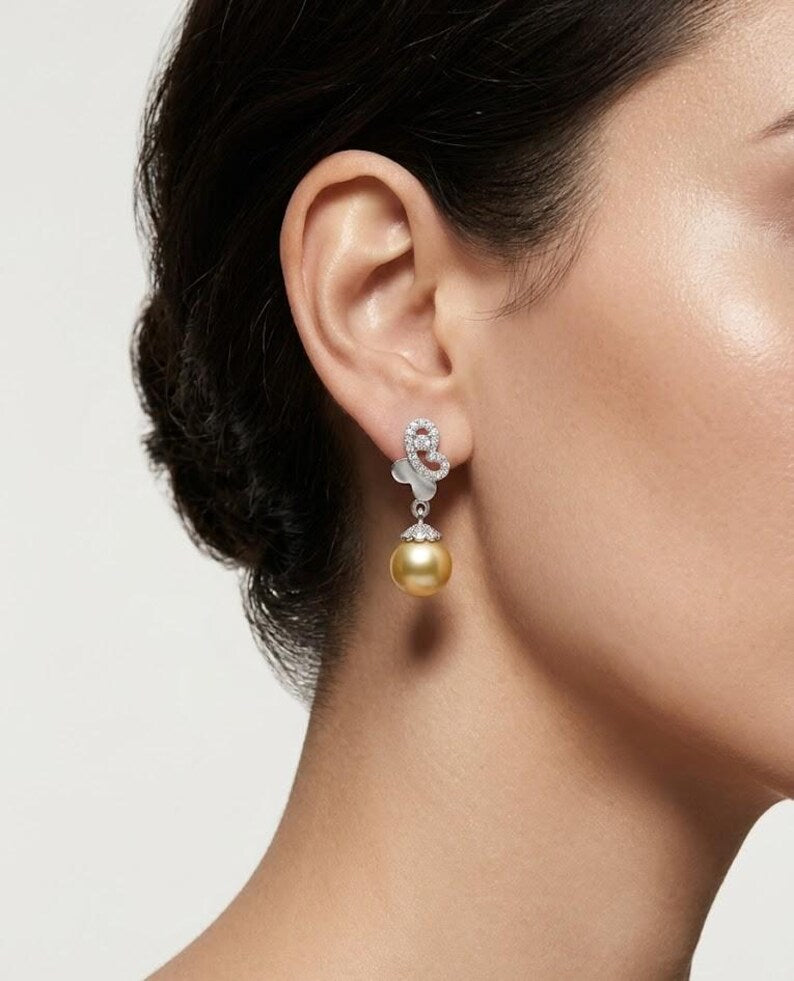 A close-up of a model's ear wearing a dangling earring with a gold pearl and silver-toned floral details.