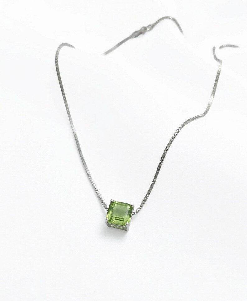 A silver chain necklace with a small square-cut green gemstone pendant, displayed on a clean white background.