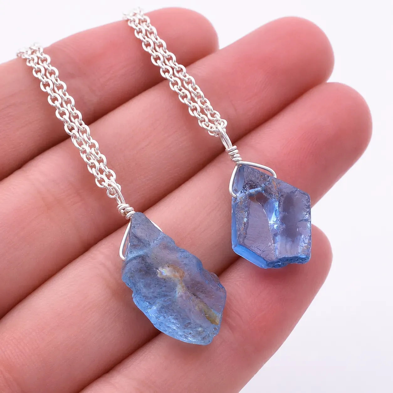 Blue crystal pendant on a silver chain held in hand against a white background