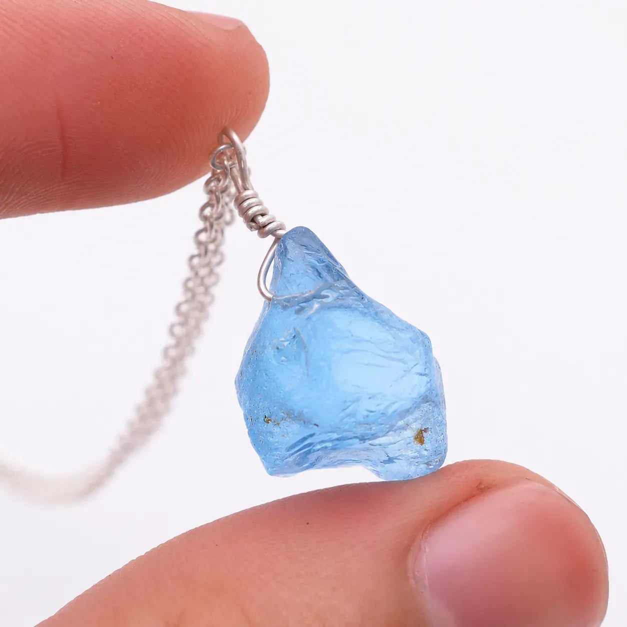Blue crystal pendant on a chain held between fingers against a white background